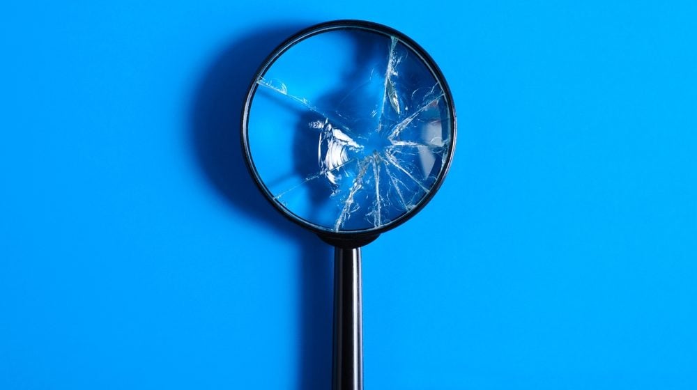 Broken magnifying glass with cracks on blue background, top view.